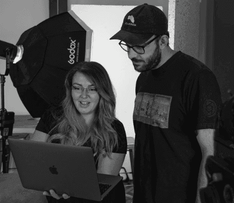 Black and white photo of two people looking at a computer screen with papers on wall